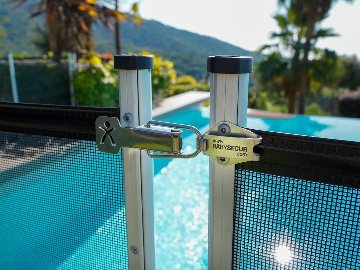 Dettaglio della chiusura di sicurezza BabySecur che unisce due pannelli della recinzione, con la piscina sullo sfondo
