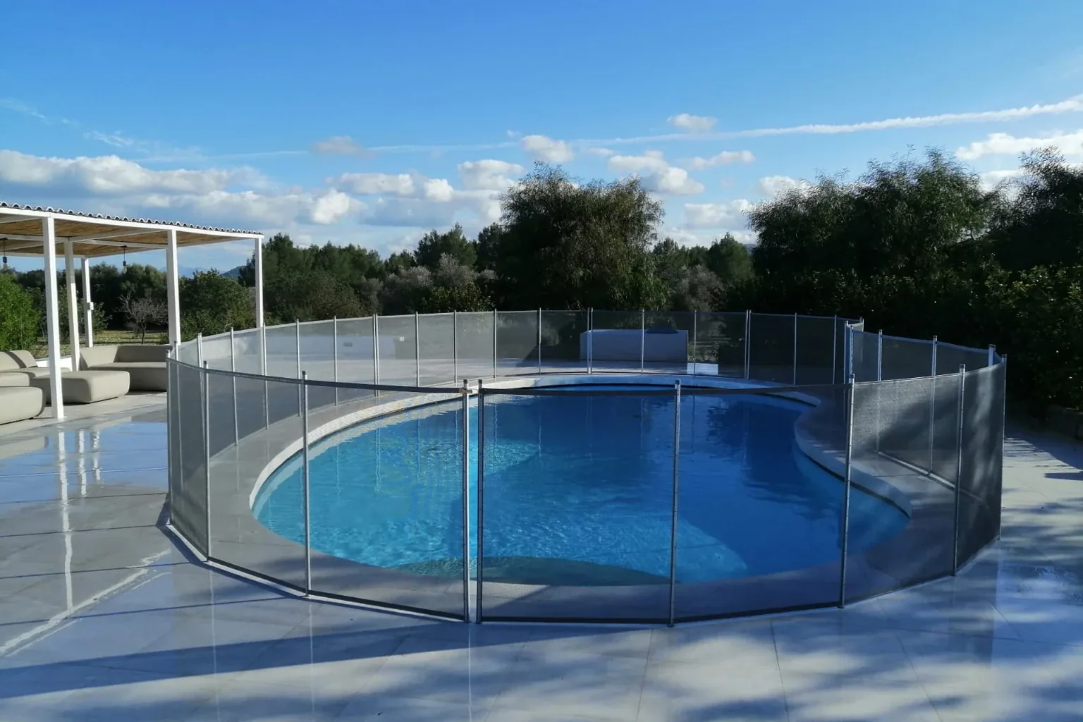 Piscina curva di una villa protetta dalla recinzione rimovibile BabySecur, con l'acqua visibile attraverso la rete