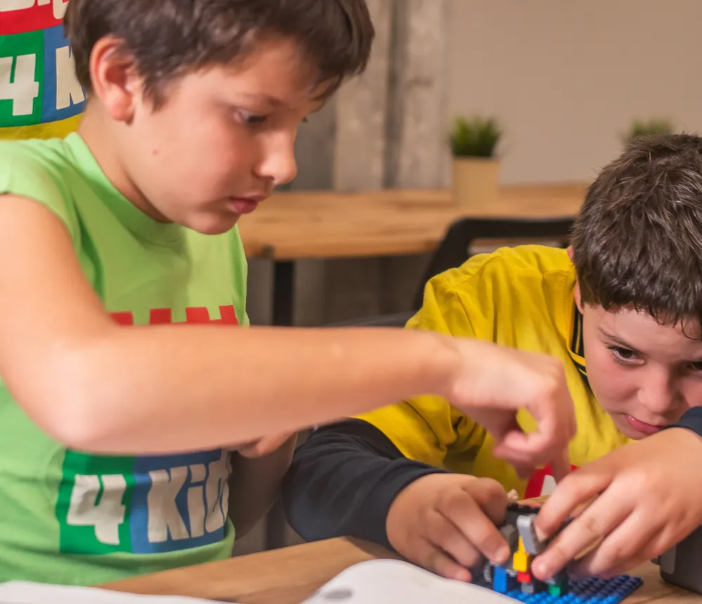 Bambini seduti al tavolo che costruiscono modelli LEGO durante un corso Bricks 4 Kidz