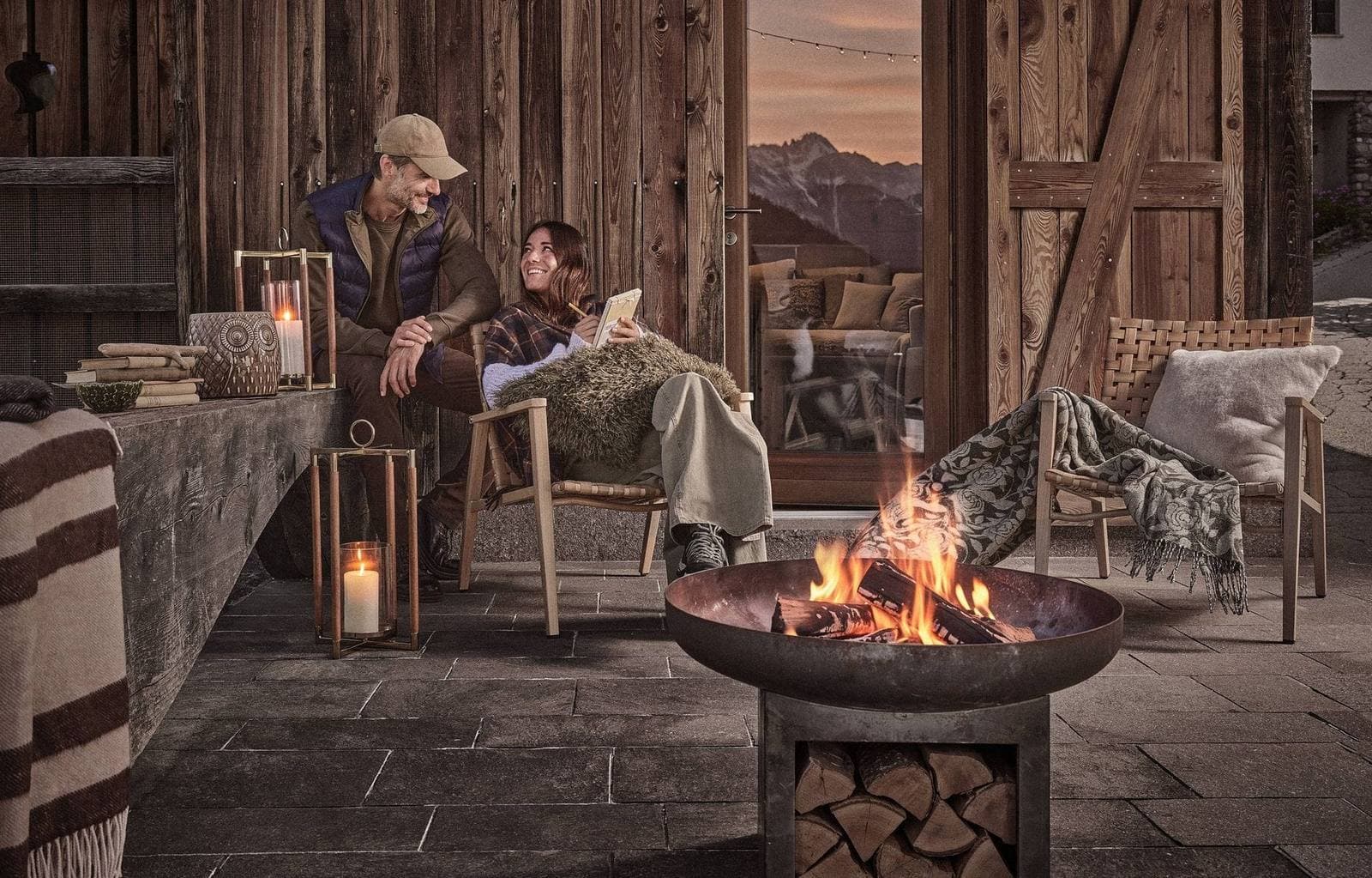 Campagna Coincasa autunno-inverno: una coppia legge accanto al fuoco in una baita, con plaid e lanterne della collezione