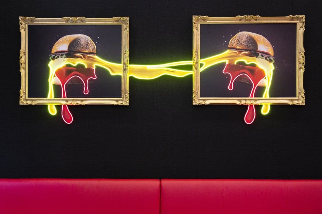 Opera pop art al neon con hamburger Cucchi Burgers, sala nera con divano rosso