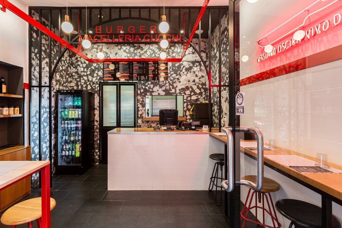 Ingresso Cucchi Burgers con arco in acciaio rosso, insegna Burger Macelleria Cucchi e pareti in terrazzo