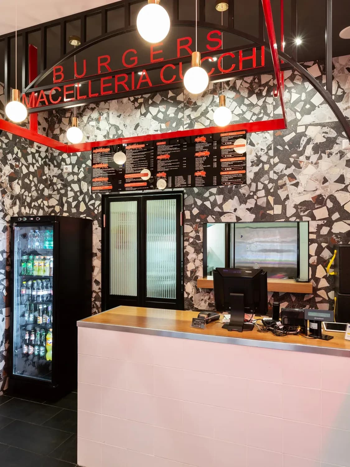 Banco Cucchi Burgers con insegna Burgers Macelleria Cucchi, pareti in terrazzo e travi in acciaio rosso