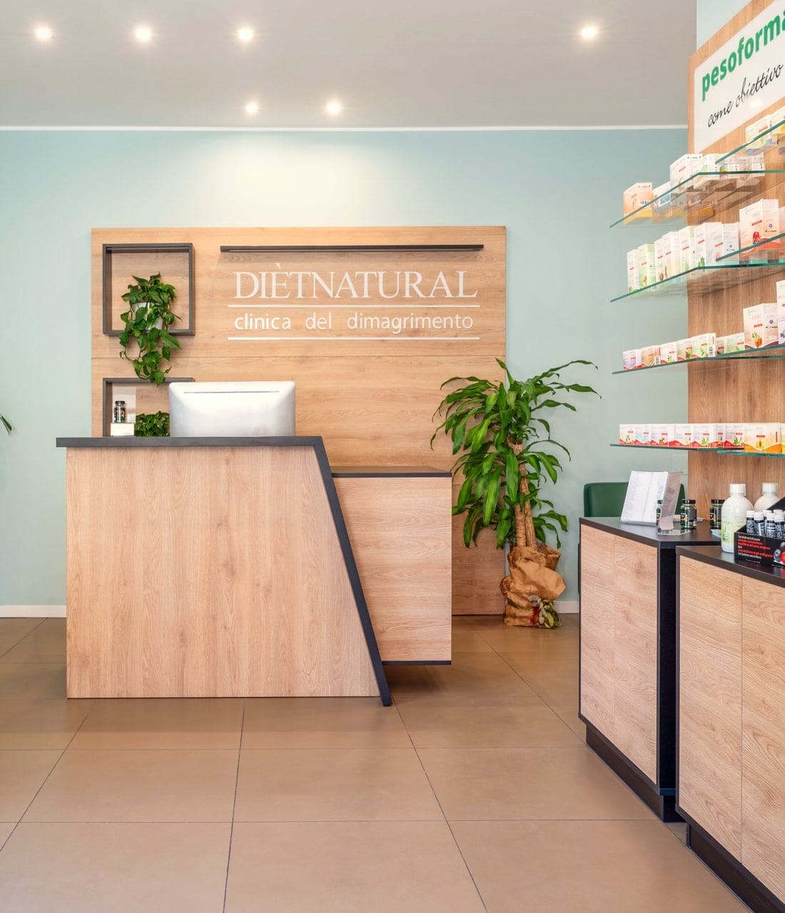 Interno di un centro Diètnatural: reception con l'insegna «clinica del dimagrimento», pareti di prodotti in rovere, piante e area d'attesa
