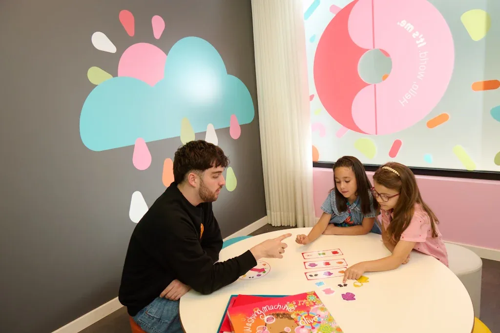 Nauczyciel Kids&Us prowadzi zajęcia po angielsku z dwiema dziewczynkami przy stole
