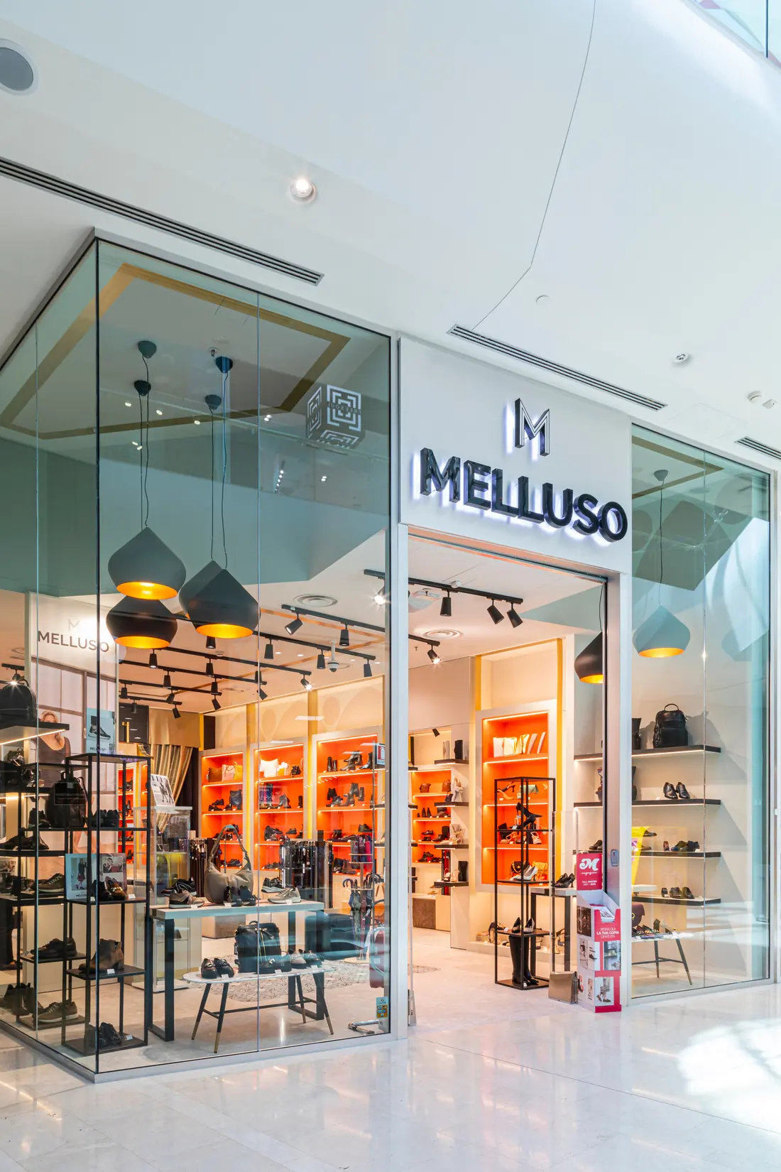 Vetrina di un negozio Melluso in un centro commerciale, con le pareti arancioni piene di scarpe e borse