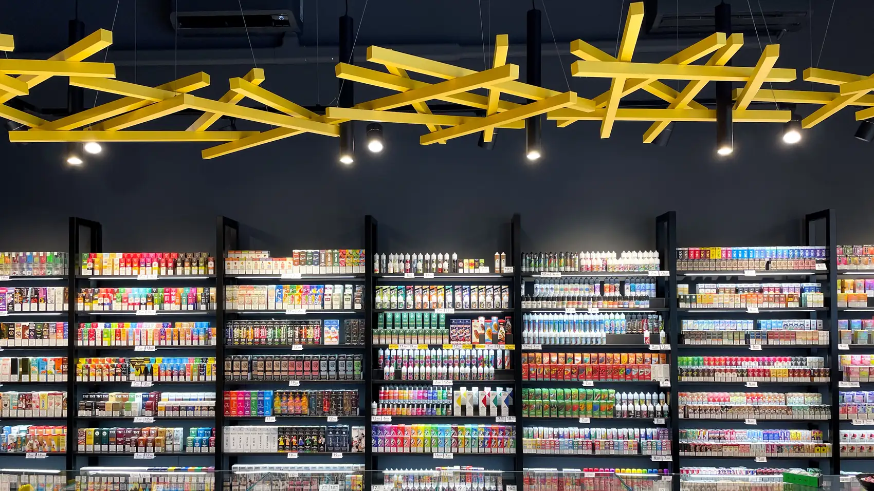 Parete di liquidi e dispositivi sotto il soffitto a travi gialle di uno Svapo&Basta Store